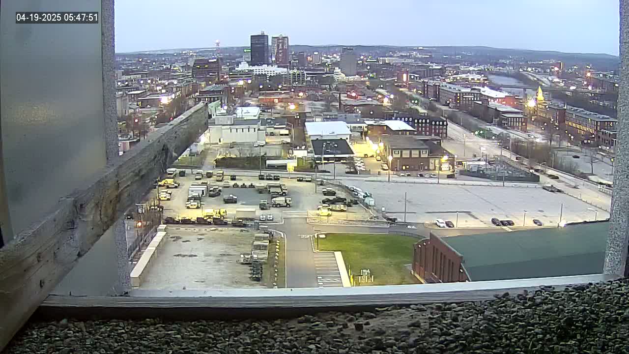 A high-angle, twilight view of a city with numerous buildings and a large parking lot containing several vehicles.