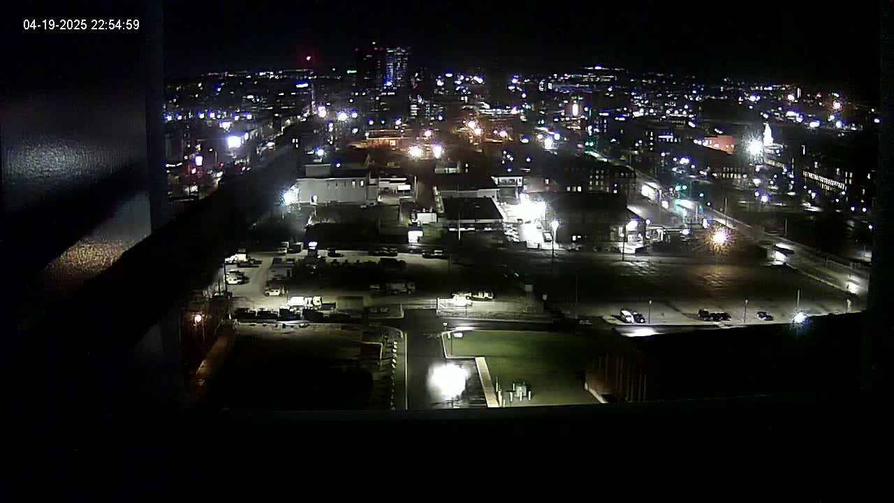 A nighttime, high-angle view of a city's industrial area and surrounding buildings, sparsely populated with vehicles.