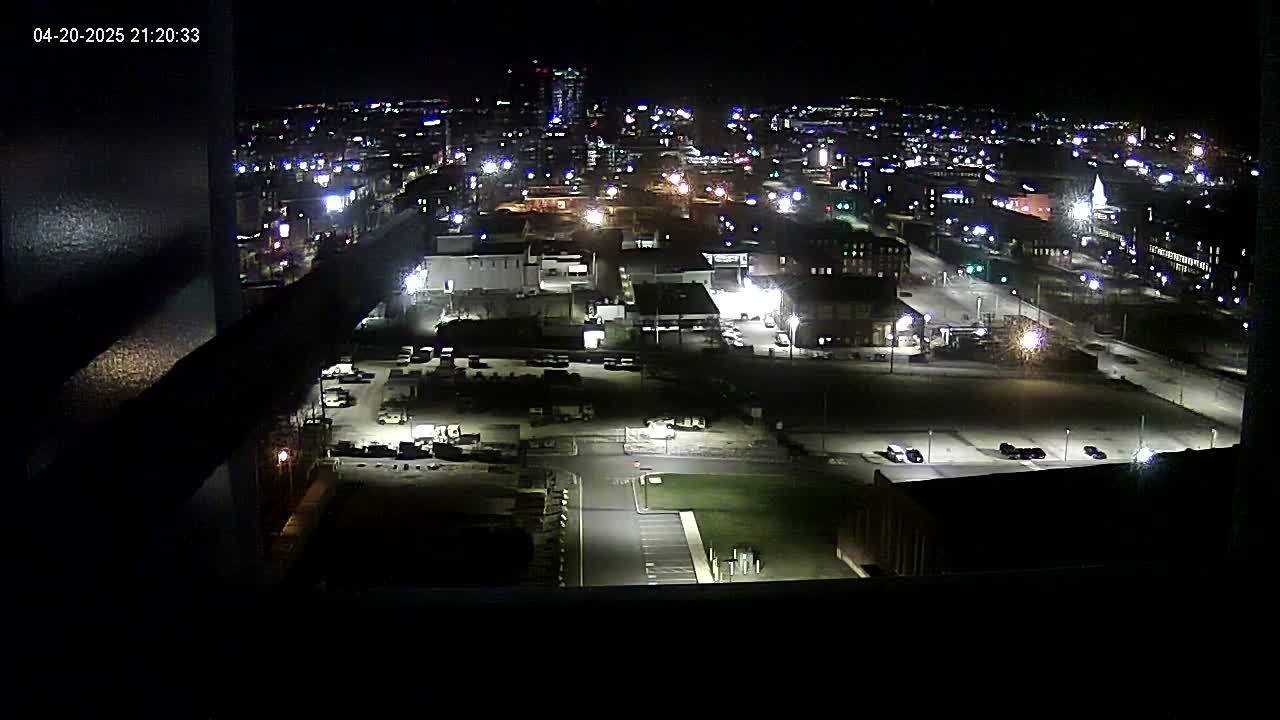 A nighttime, high-angle view of a city's industrial area with numerous buildings and parking lots illuminated by artificial lights.