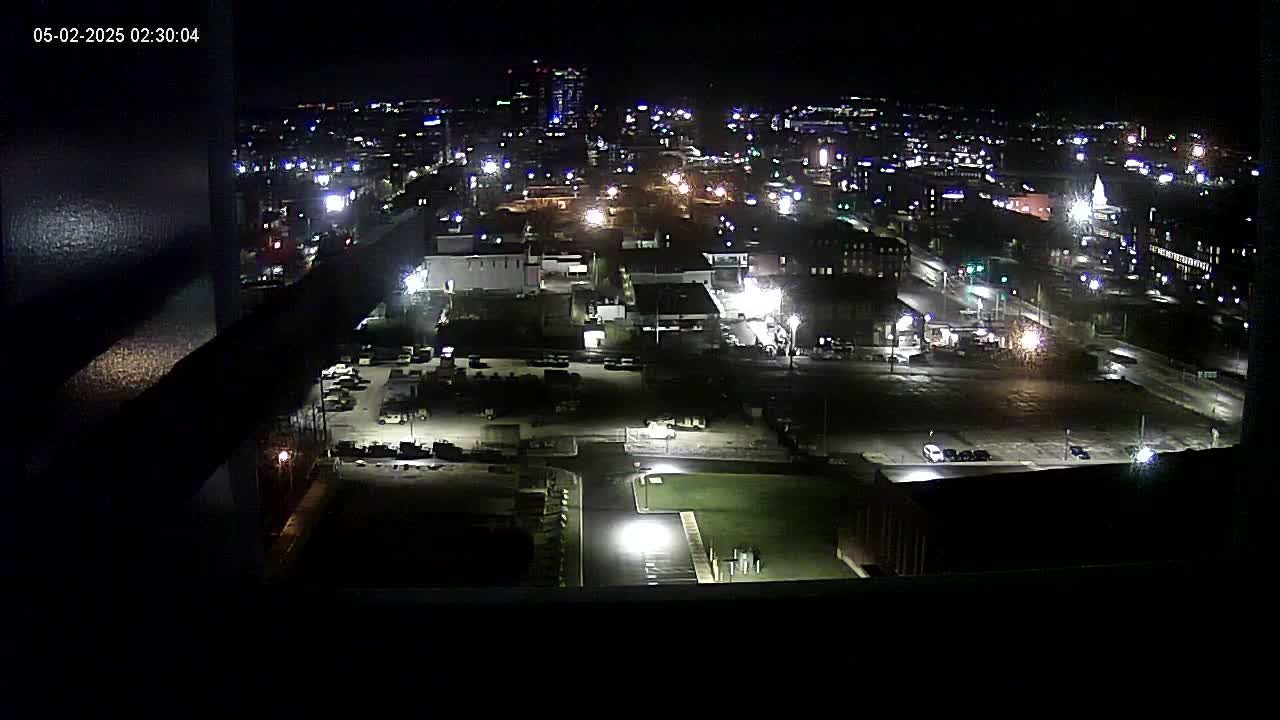 A nighttime high-angle view of a city illuminated by streetlights and building lights, showing a mix of parking lots and buildings.