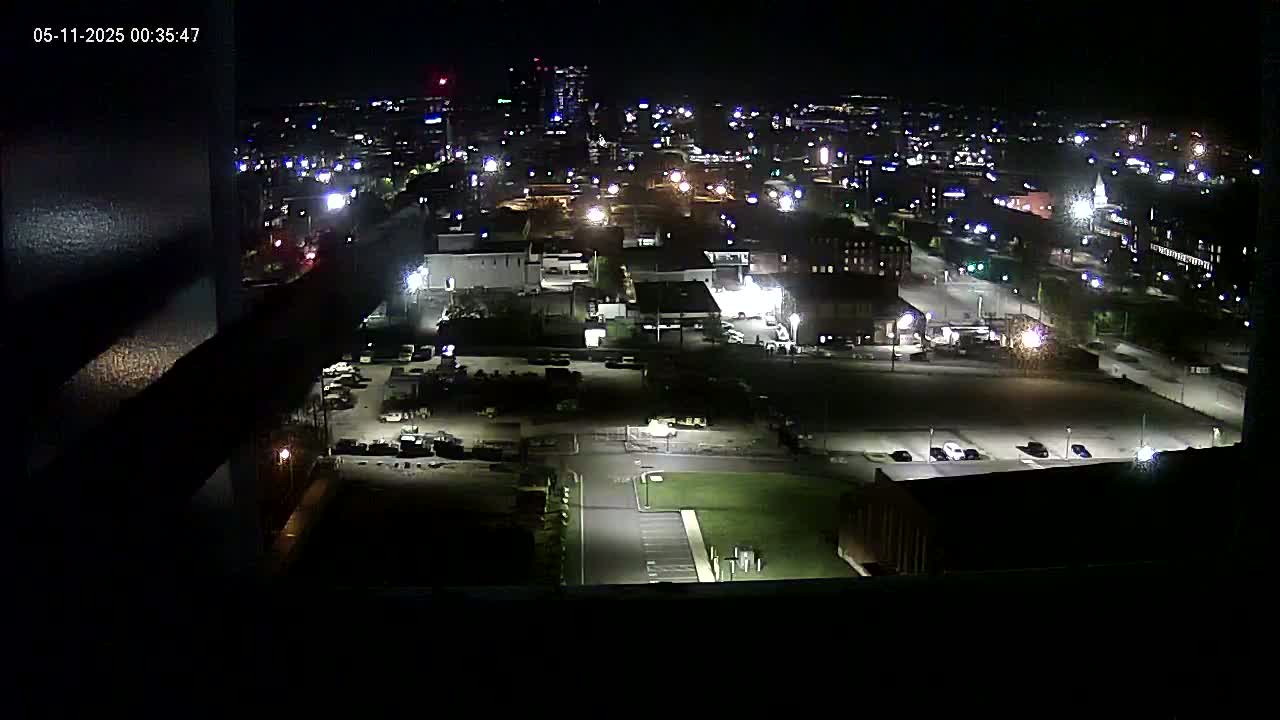 A nighttime, high-angle view of a city's industrial and residential areas, illuminated by streetlights and building lights.