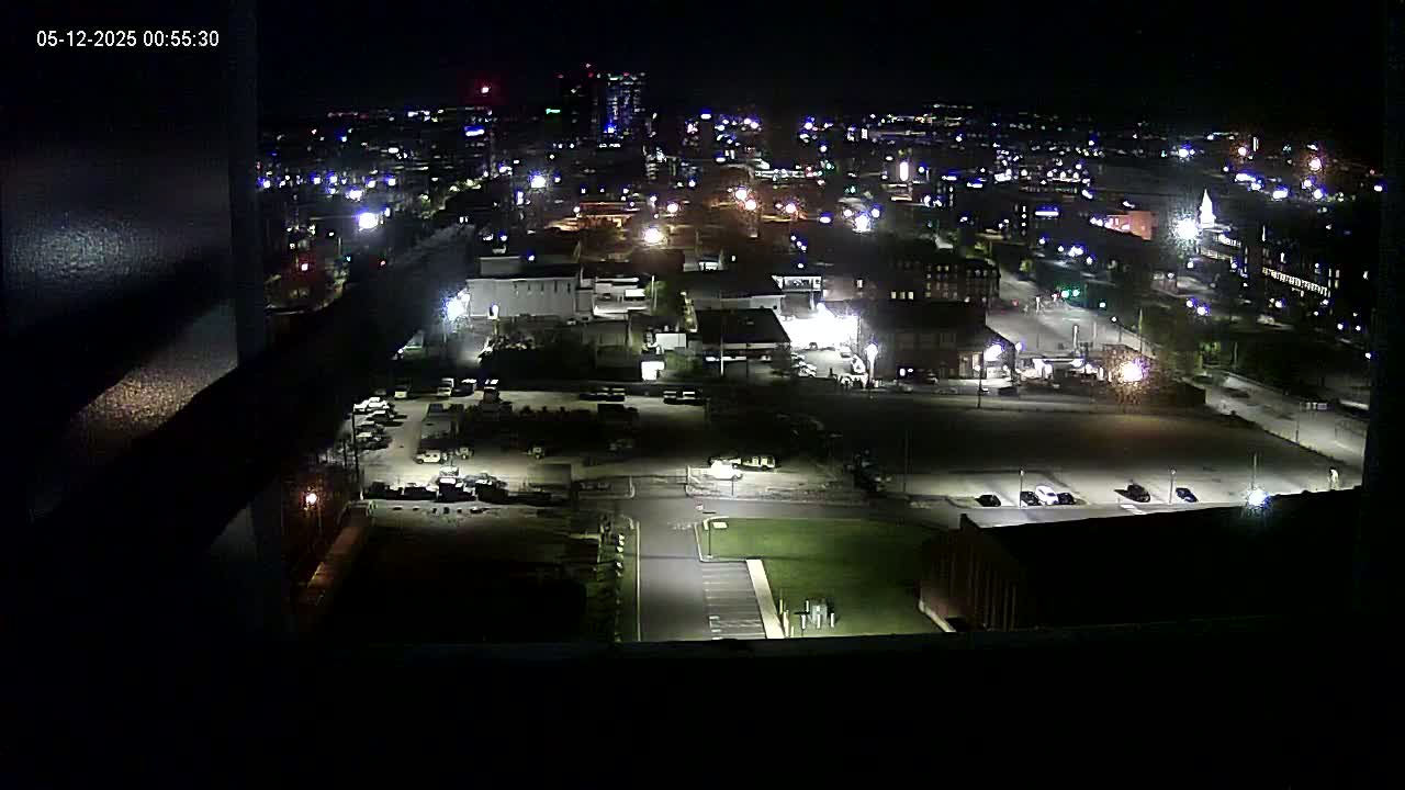 A nighttime, high-angle view of a city's industrial area with sparsely parked cars and buildings illuminated by streetlights.