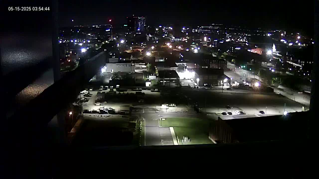A nighttime, high-angle view of a city's illuminated streets, buildings, and parking lots.