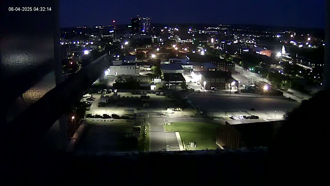 A nighttime, high-angle view of a city's industrial and residential areas, illuminated by streetlights and building lights.