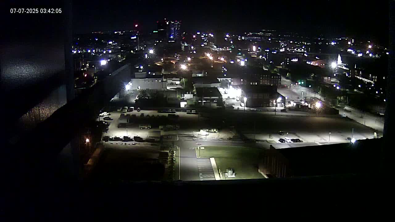 A nighttime high-angle view of a city's industrial area and surrounding buildings, illuminated by streetlights and building lights.