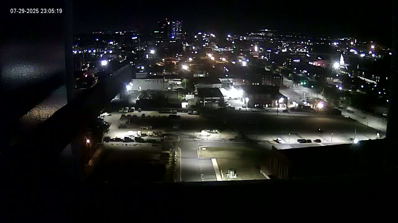 A nighttime aerial view of a city, showing dimly lit streets, buildings, and parking lots.