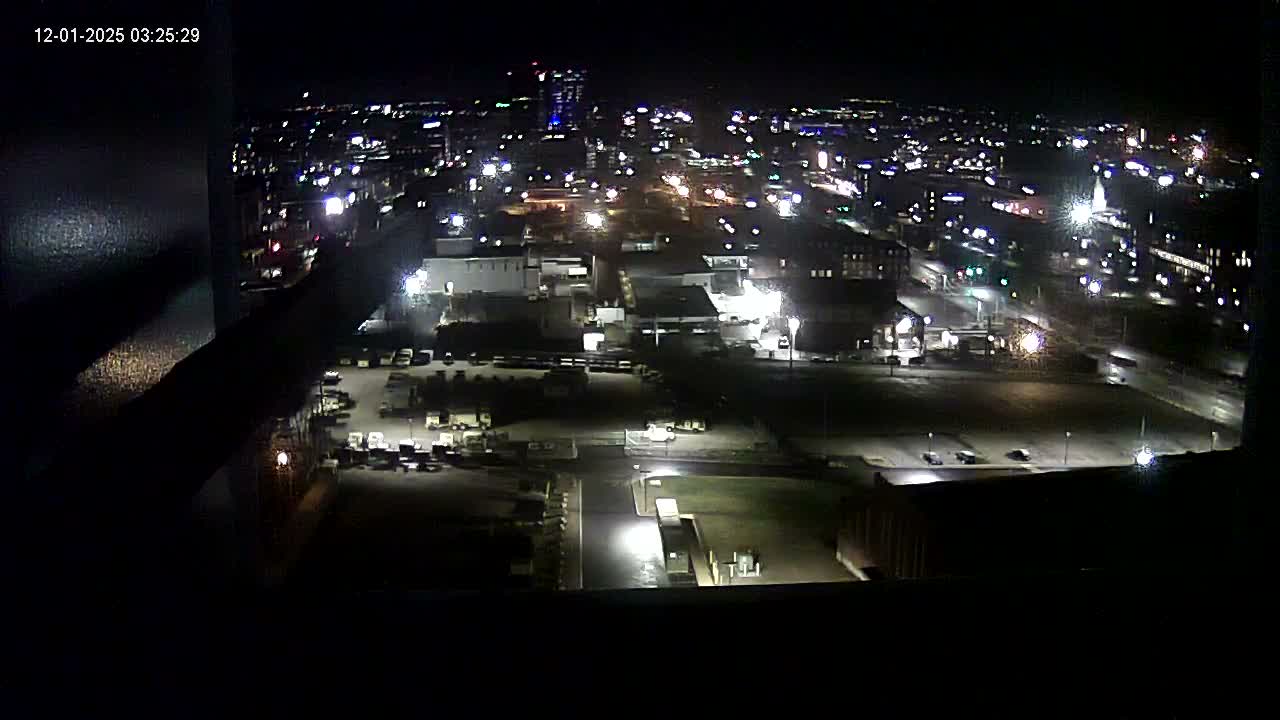 An aerial view captures a sprawling city at night, brightly illuminated by numerous streetlights and building lights under clear, dark skies.