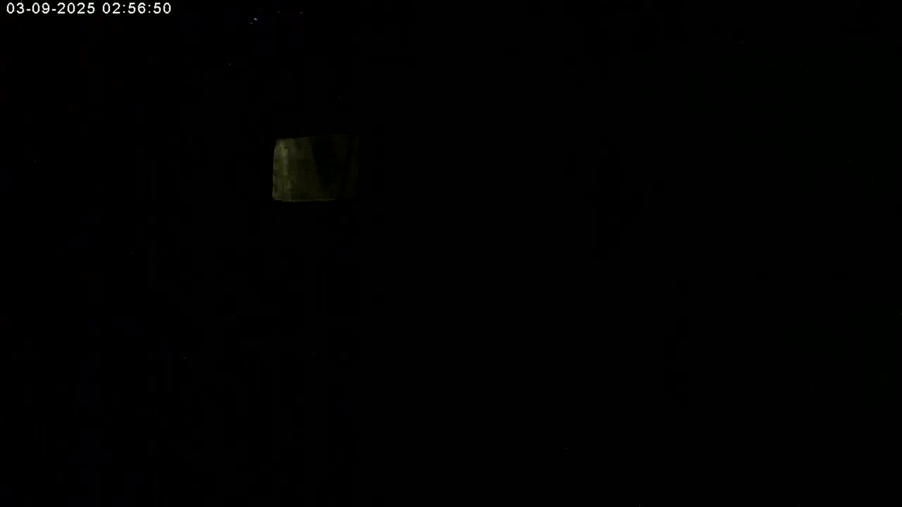 A dimly lit, dark scene shows a small, faintly illuminated rectangular object in the upper left corner.