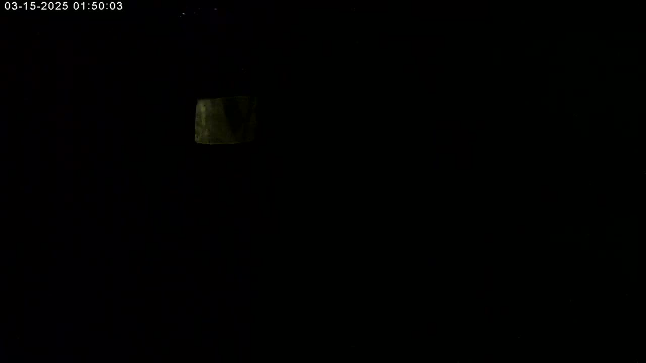 A dimly lit, dark scene shows a small, indistinct, light-colored rectangular object in the upper left corner.