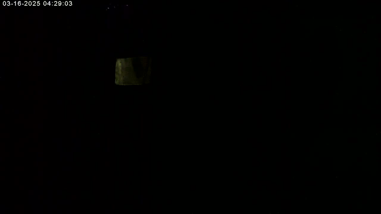 A dimly lit, mostly dark scene shows a small, indistinct, light-colored object in the upper left corner.