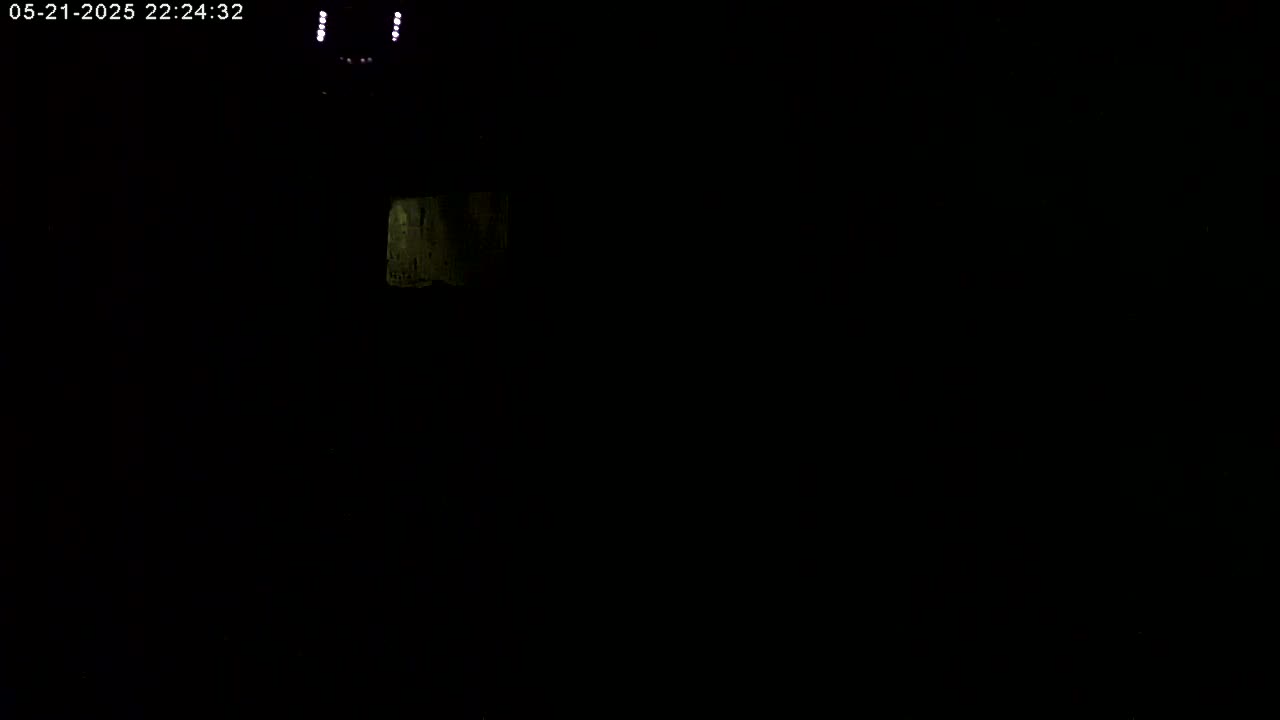 A dimly lit, dark interior scene shows a small section of a pale surface in the upper left corner.
