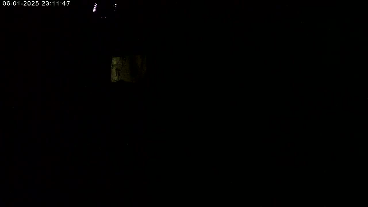 A dimly lit, dark scene shows a small, faintly illuminated section of a wall or surface.