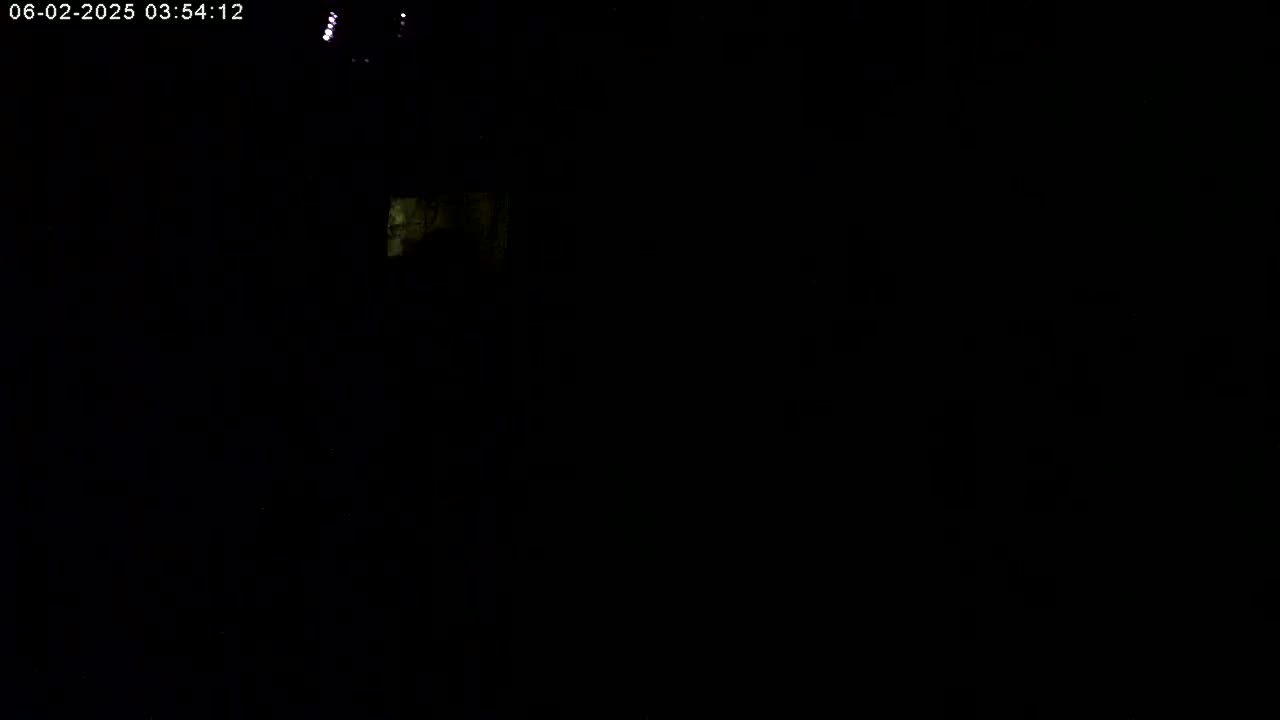 A dimly lit, mostly dark scene at night shows a small, faintly illuminated area in the upper left corner.