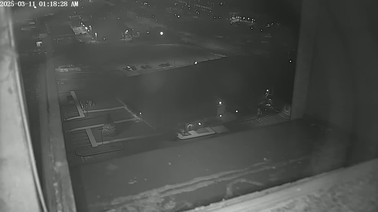 A nighttime, high-angle view from a window shows a parking lot and building exterior, illuminated by artificial lights.