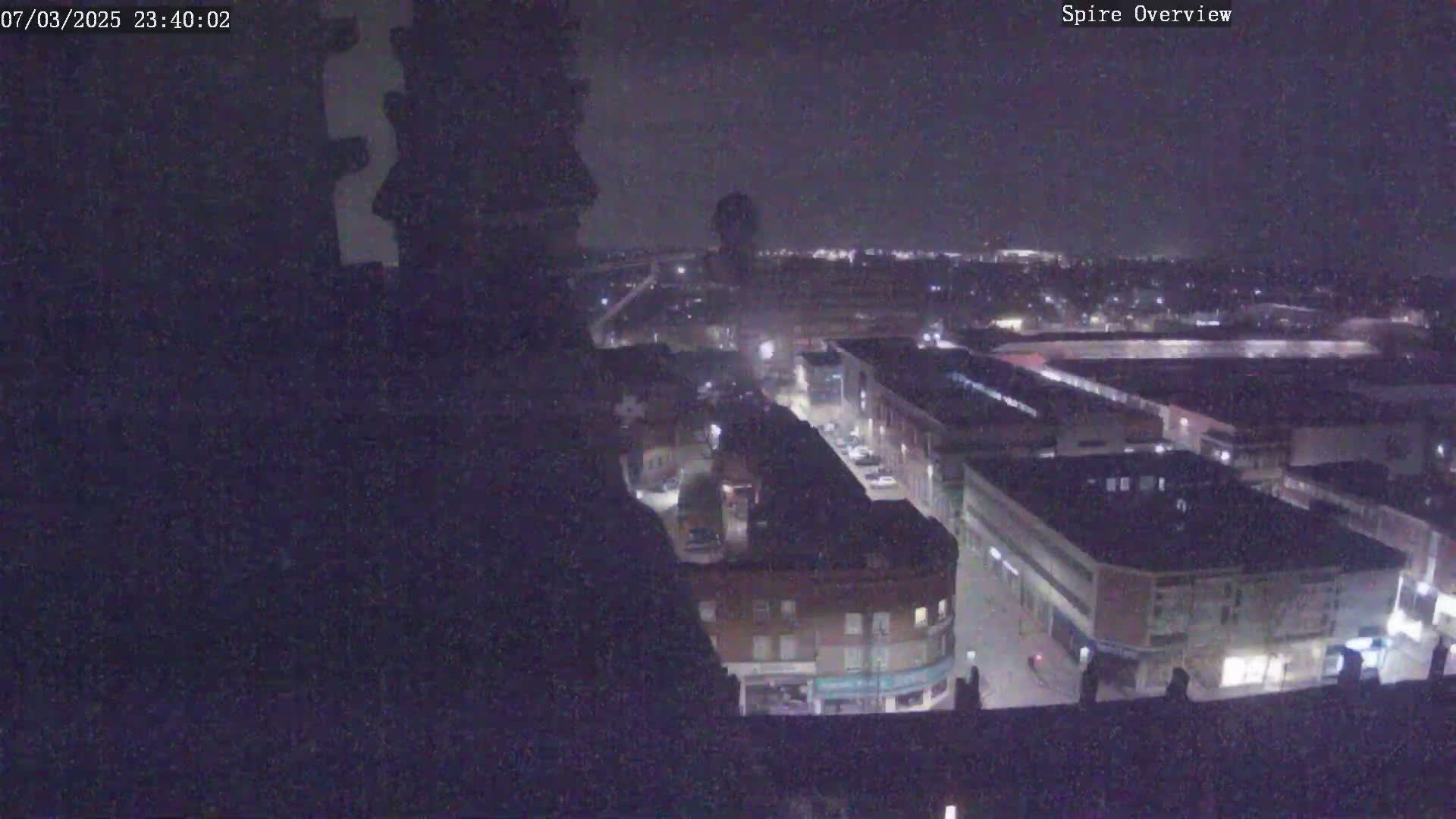 A nighttime, high-angle view of a city block showing buildings and streets illuminated by artificial light.