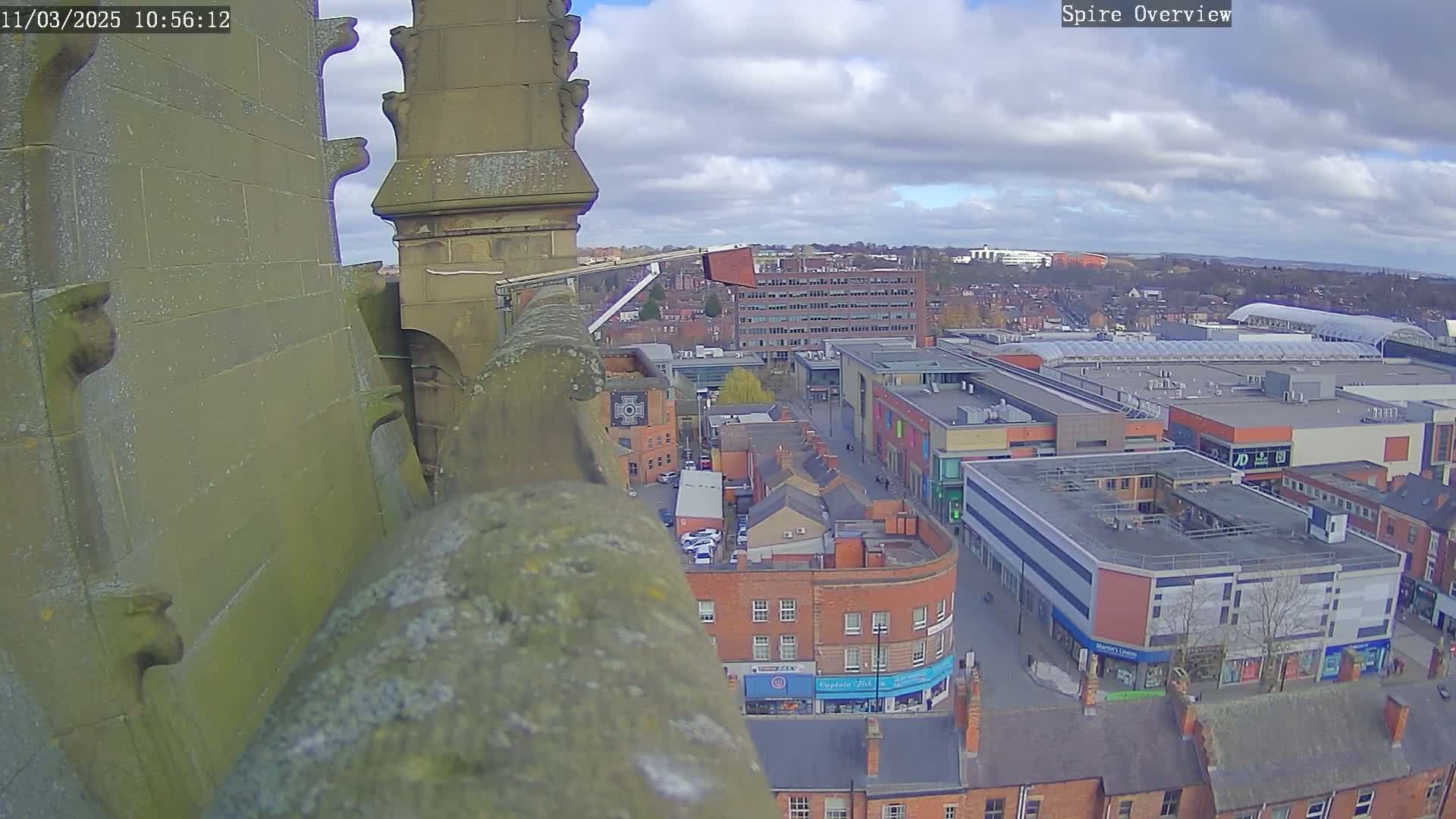 A high-angle view from a stone structure shows a town center under a partly cloudy sky.