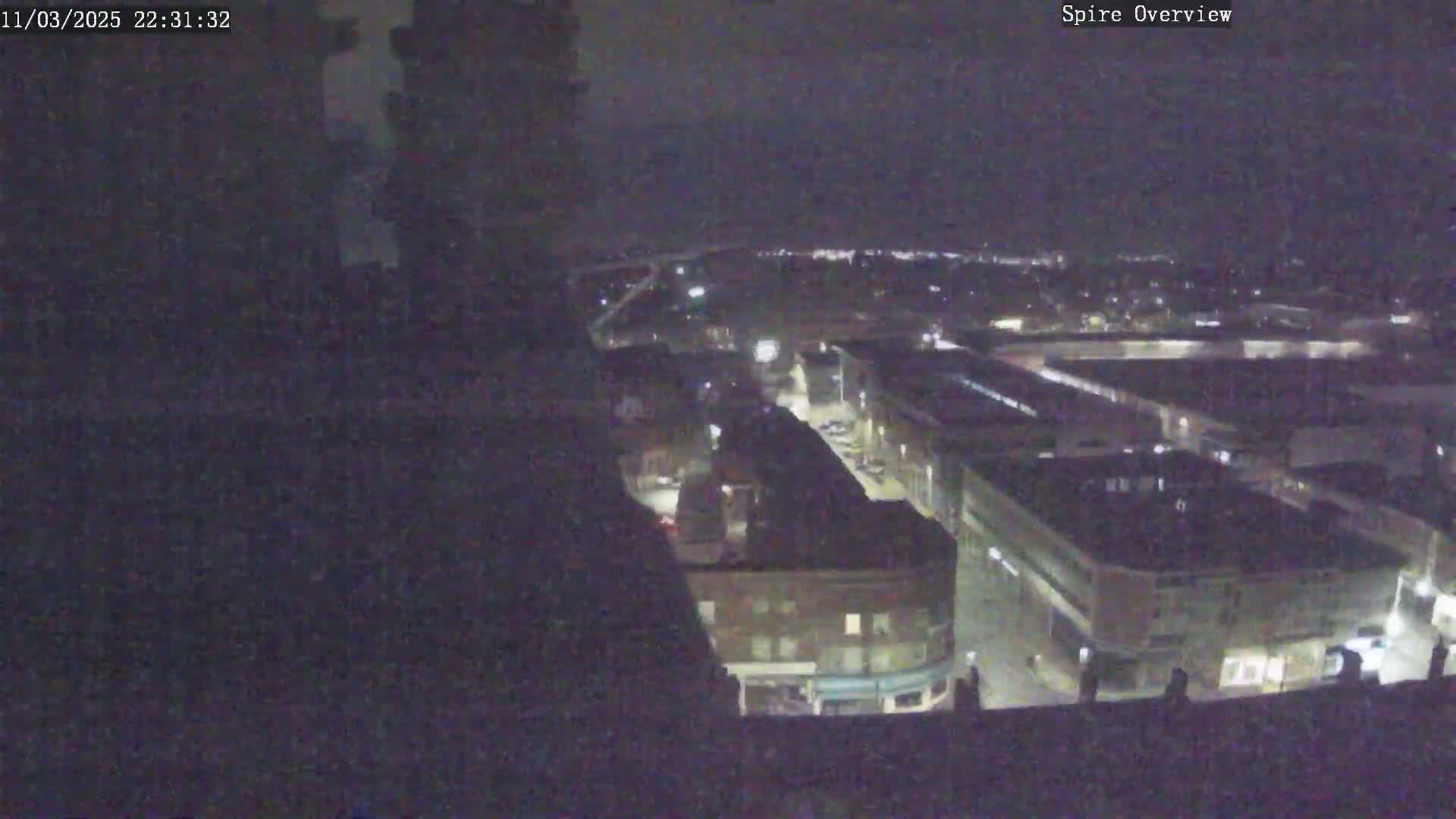 A nighttime high-angle view shows a city block with several buildings illuminated under a dark sky.