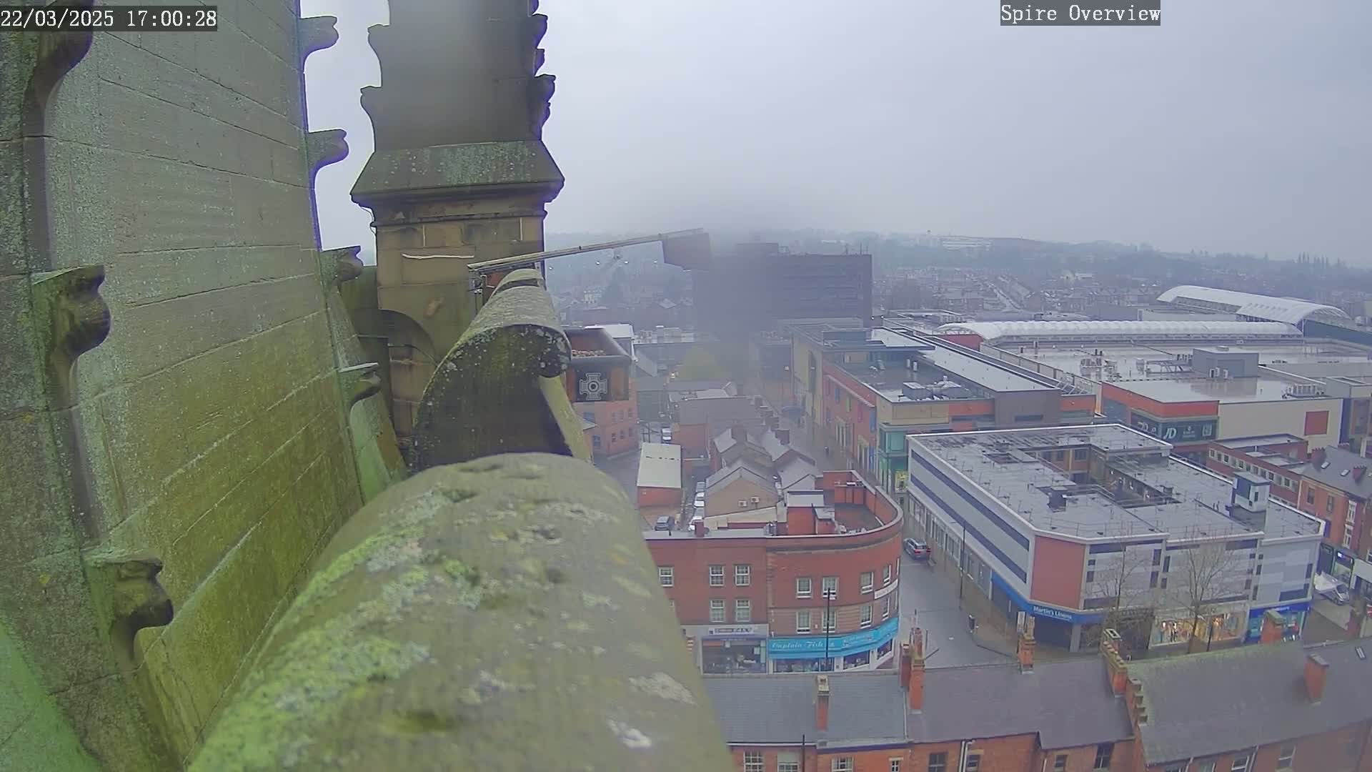 A high-angle view from a stone spire shows a city on an overcast day, with buildings and streets visible below.