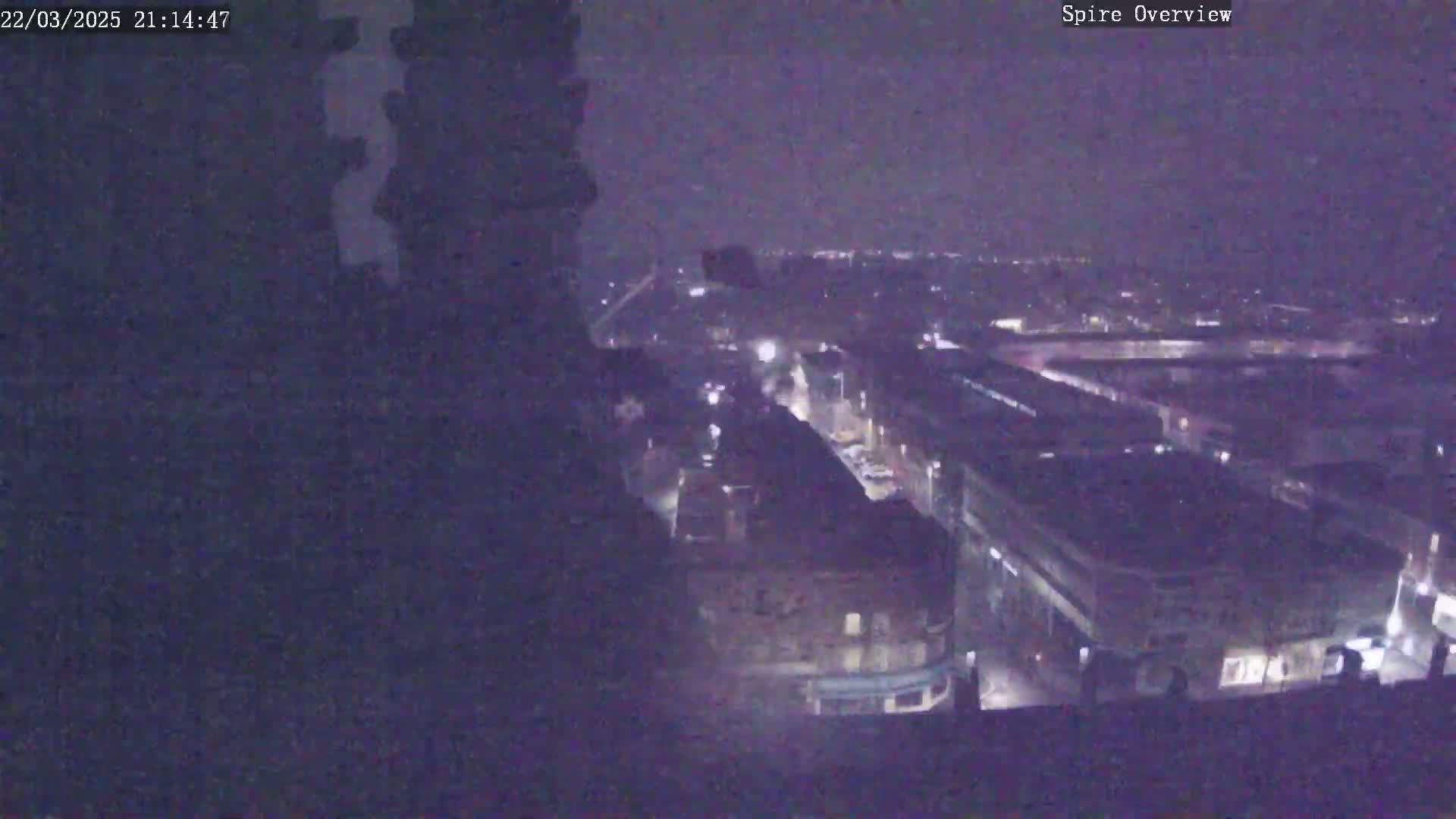 A nighttime, high-angle view shows a city with dimly lit streets and buildings under a dark sky.