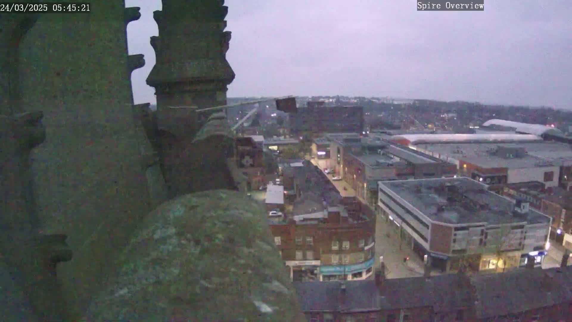 A high-angle, twilight view from a stone structure shows a city with buildings and streets below under a cloudy sky.