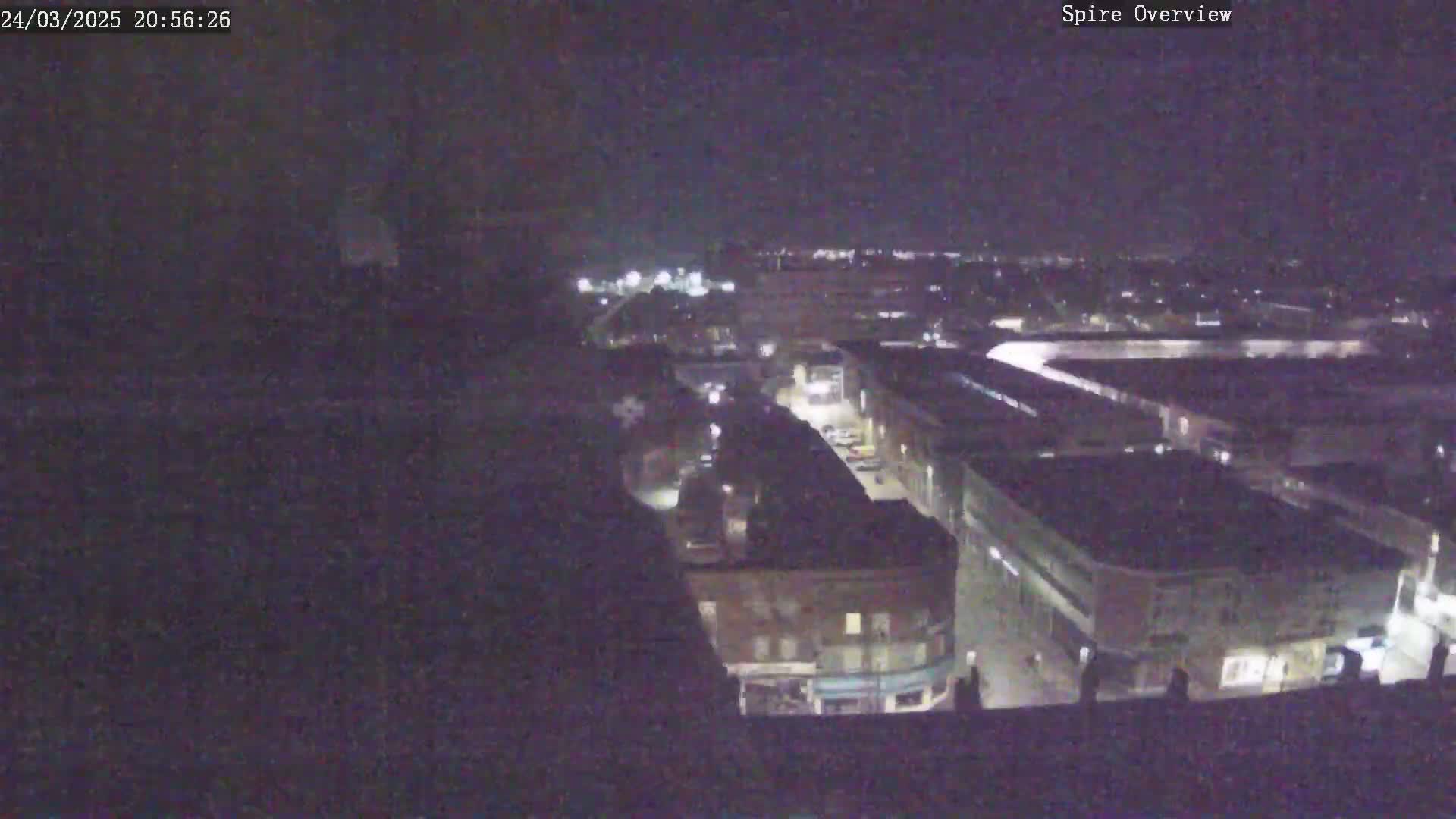 A nighttime aerial view shows a city block with several buildings and streets, under a dark sky.