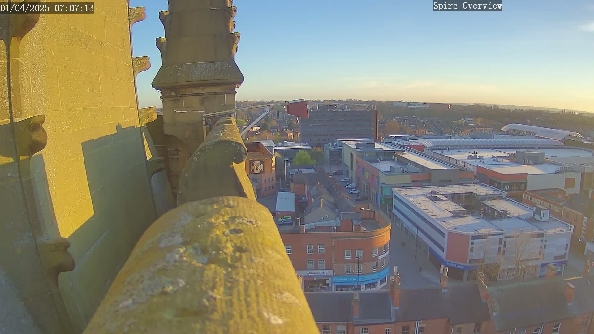 A high-angle view from a stone structure shows a city skyline under a clear, bright sky at sunset.