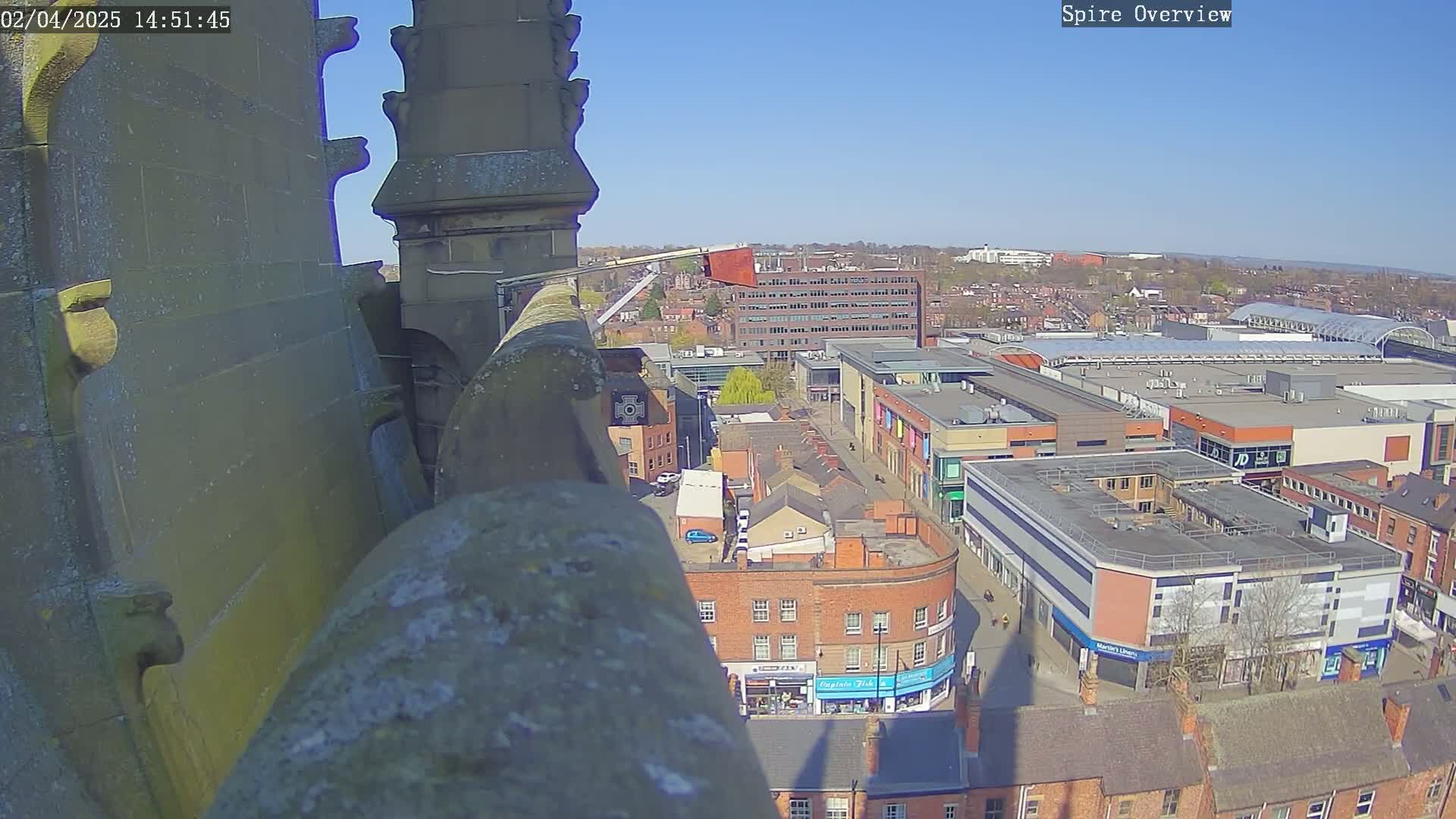 A high-angle view from a stone structure on a sunny day shows a city center with buildings, streets, and a shopping mall.