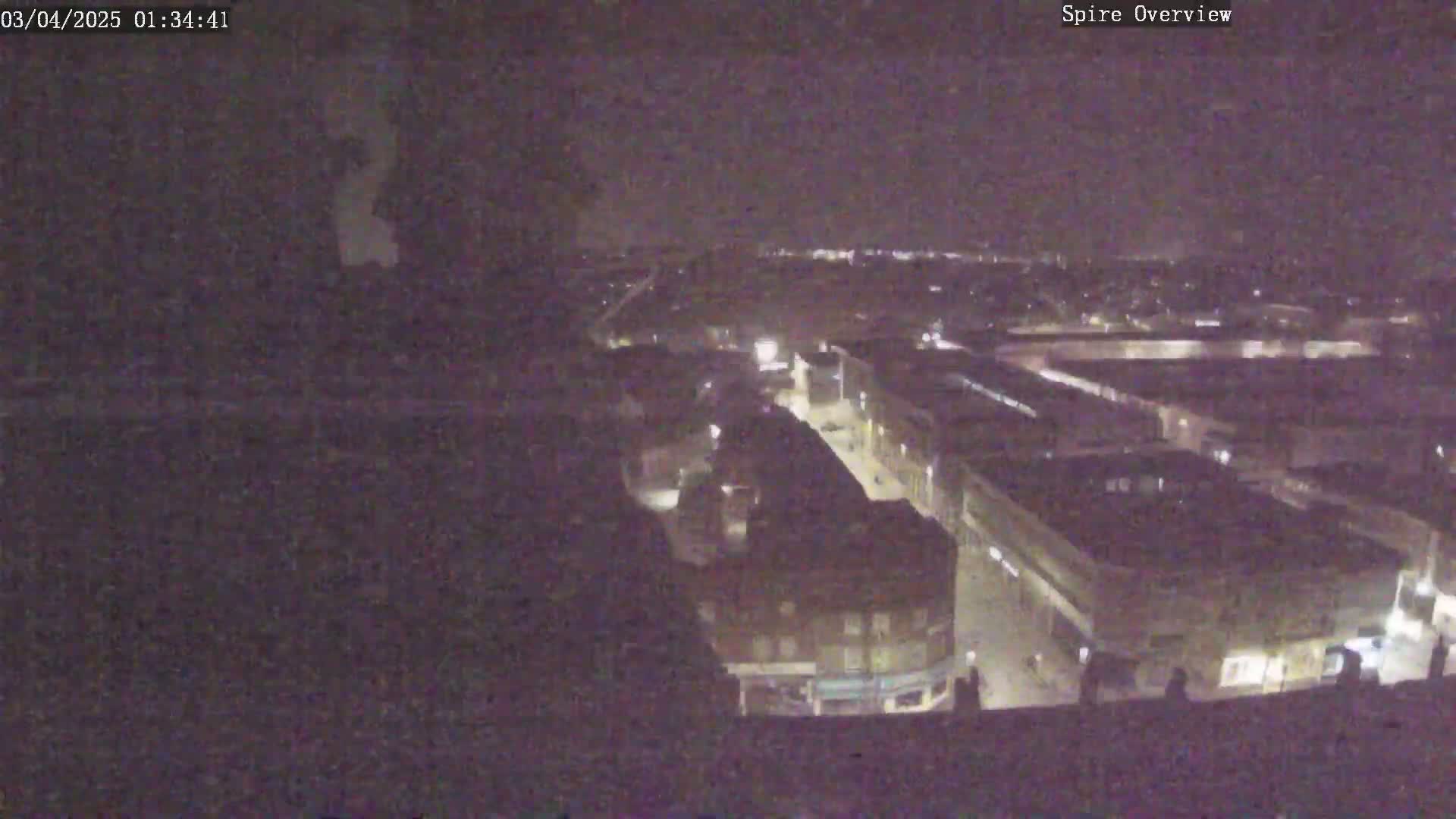 A nighttime, high-angle view shows a town's street layout with dimly lit buildings and streets.
