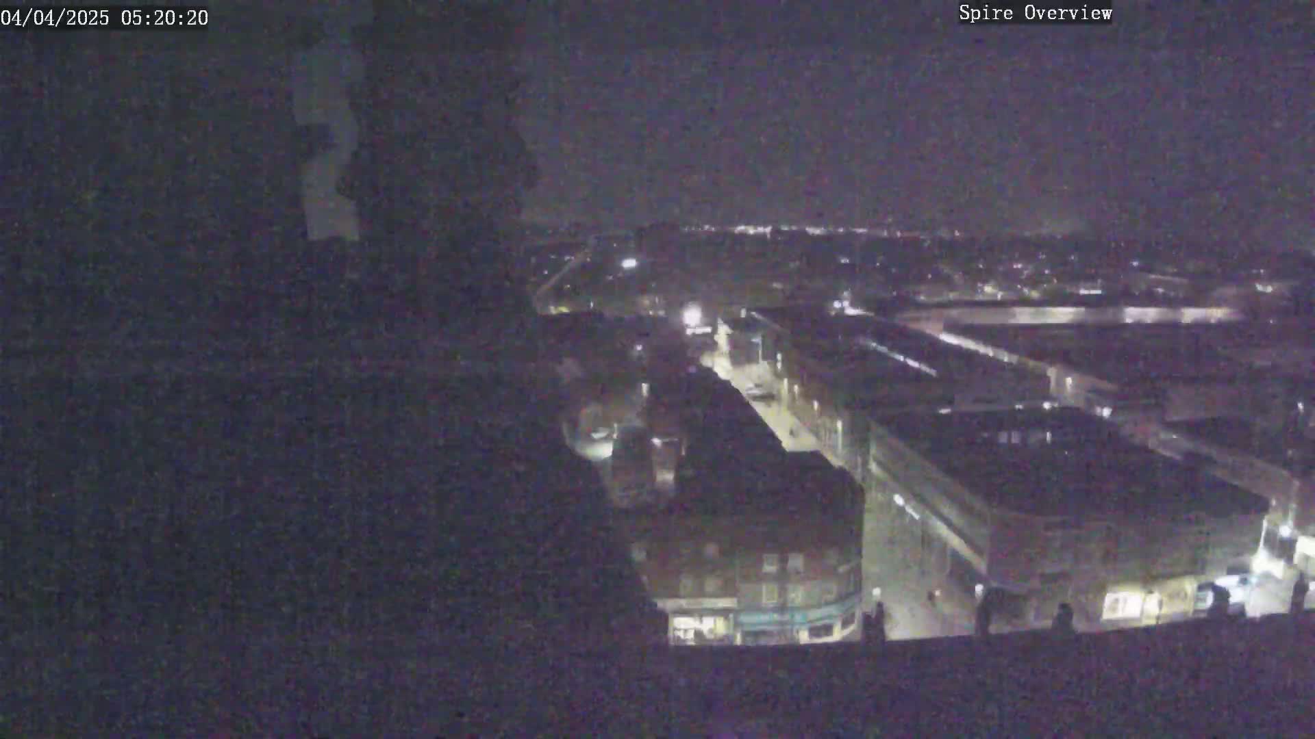 A nighttime aerial view shows a city with dimly lit streets and buildings under a clear, dark sky.