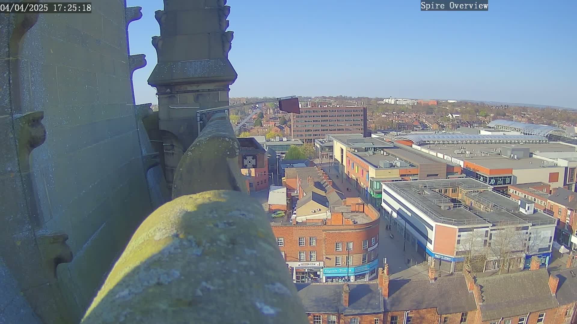 A high-angle view from a stone structure on a sunny day shows a city with a shopping center and other buildings.