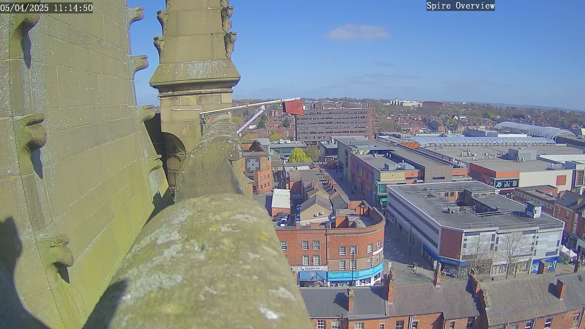 A high-angle view from a stone spire shows a town square with shops and buildings under a clear, sunny sky.