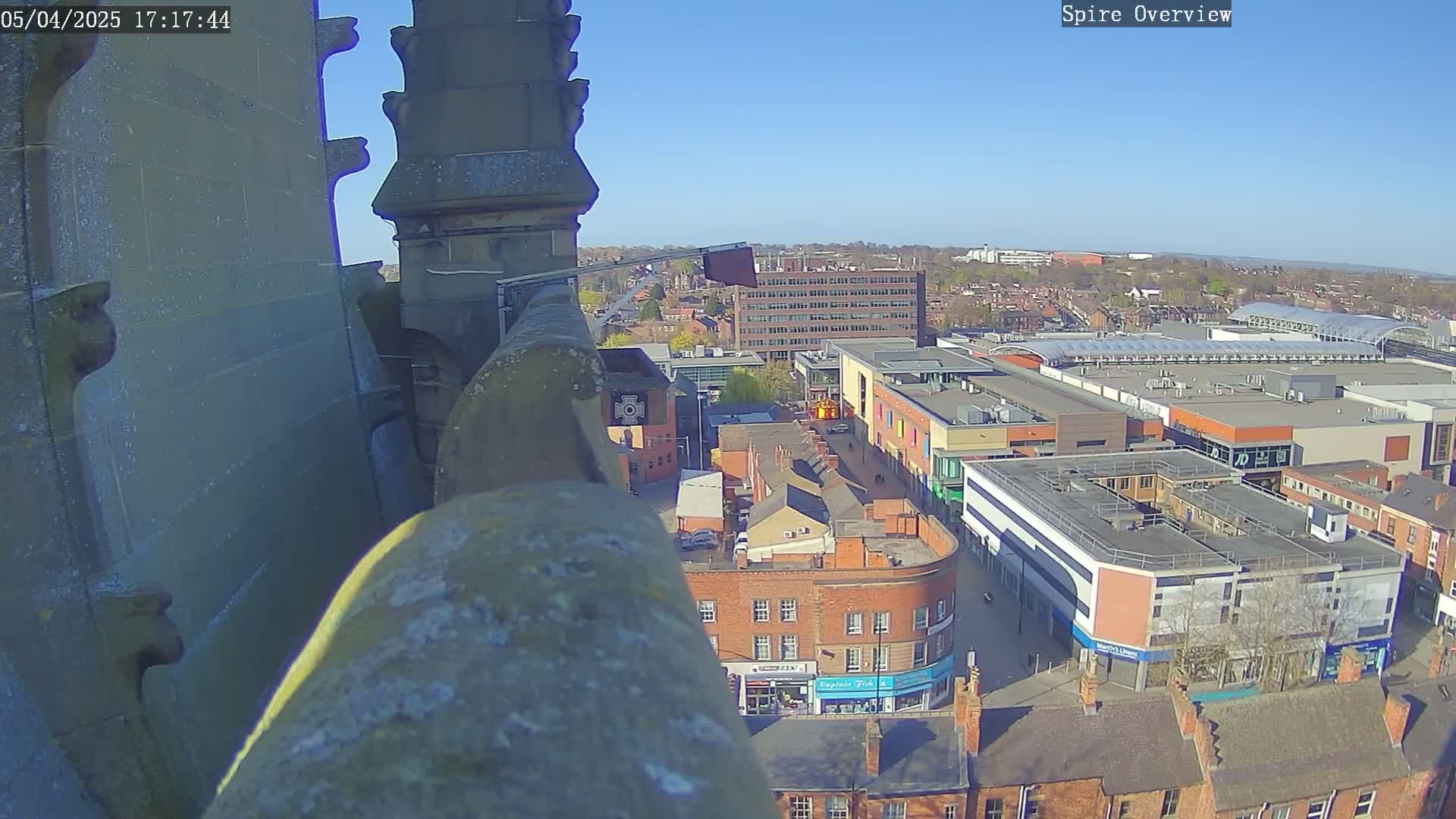 A high-angle view from a stone structure on a sunny day shows a city's streets and a shopping center below.