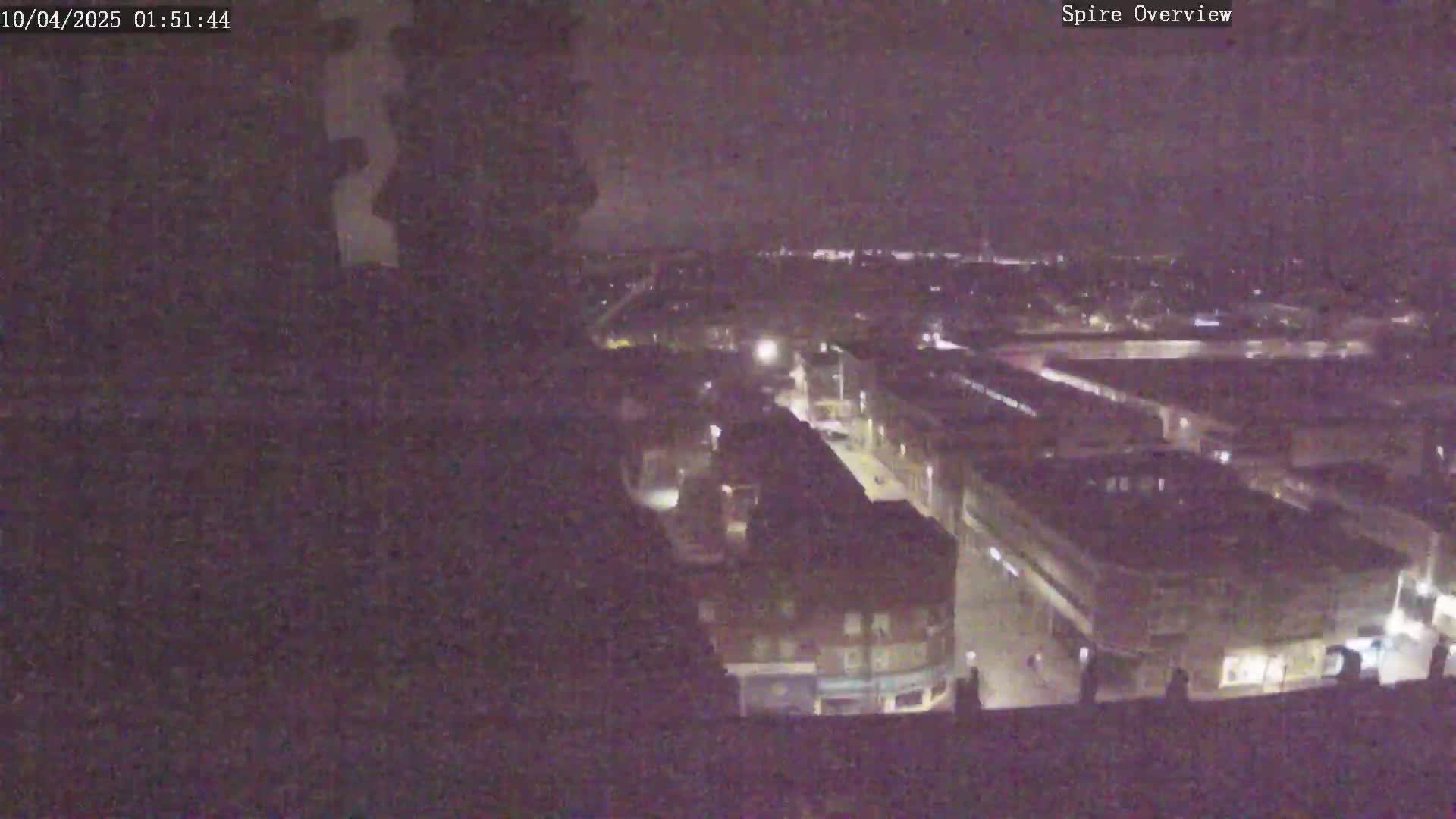A nighttime, high-angle view shows a city street and surrounding buildings dimly lit under a dark sky.