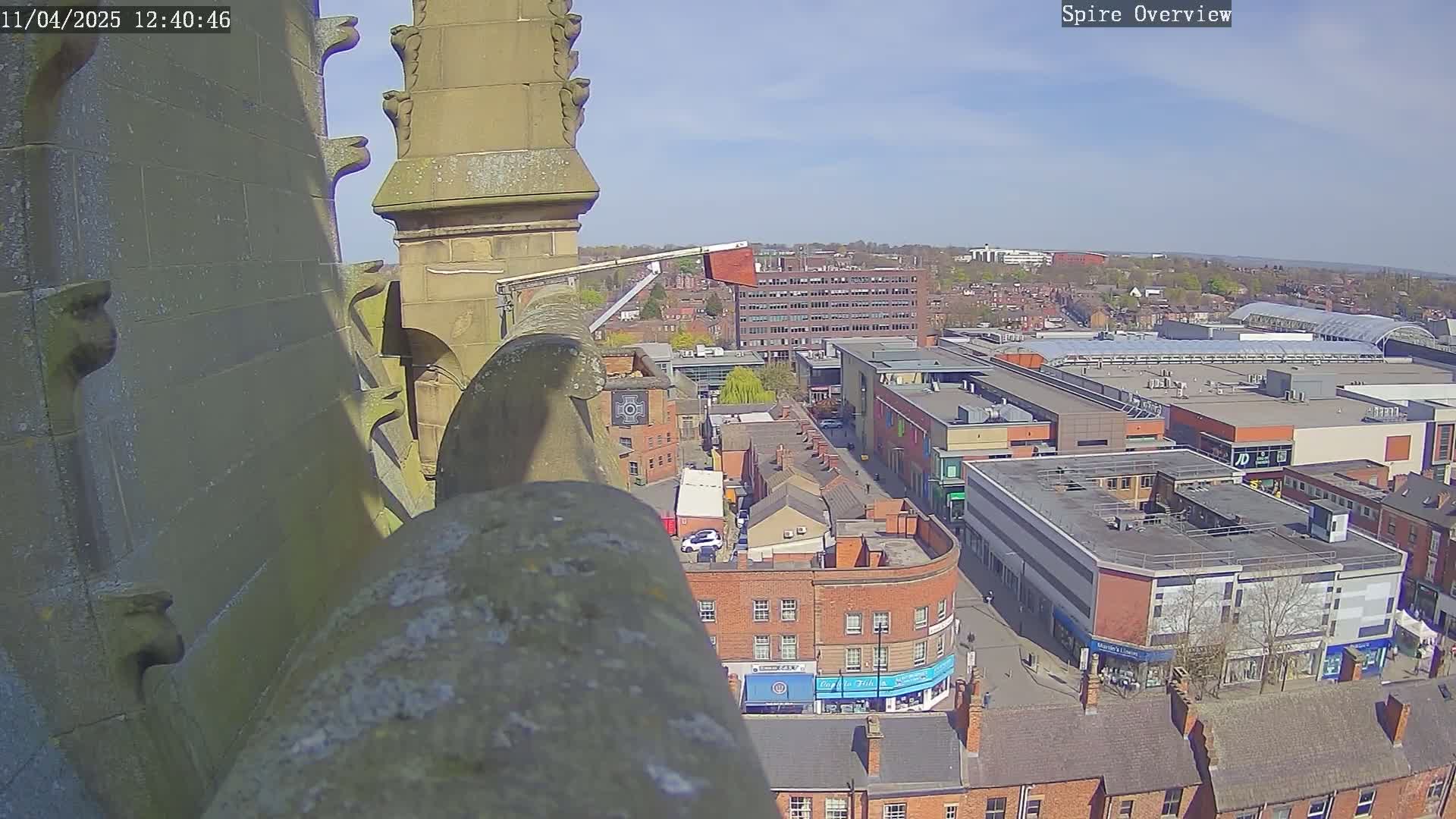 A high-angle view from a stone spire shows a town square with shops and buildings under a clear, sunny sky.