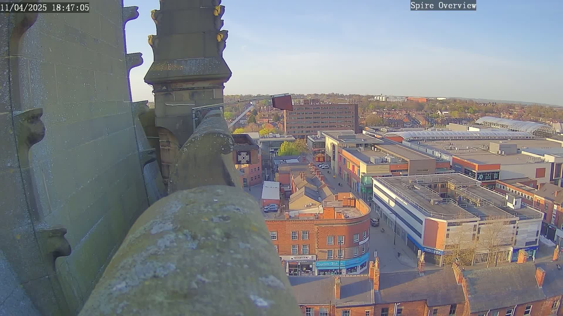 A high-angle view from a stone structure shows a town square with buildings under a clear, bright sky.