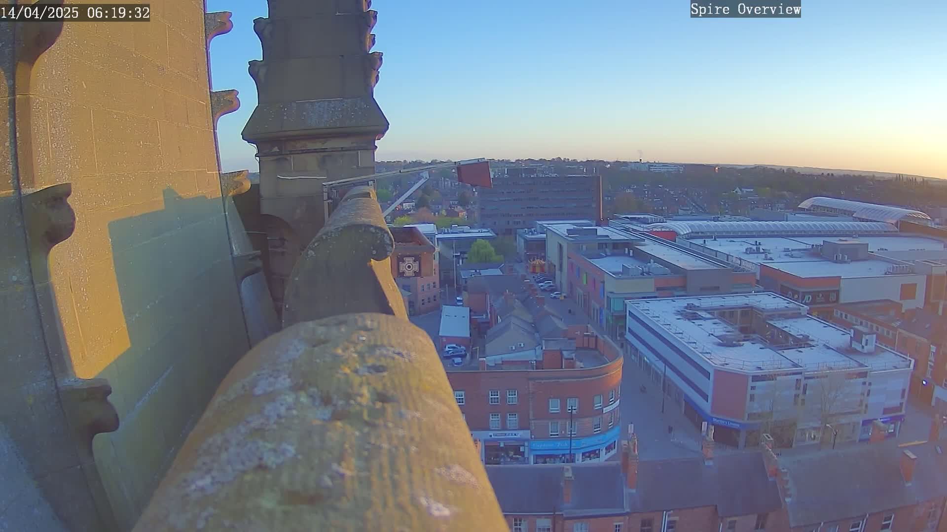 A high-angle view from a stone structure at sunrise shows a town with a shopping center, under a clear sky.
