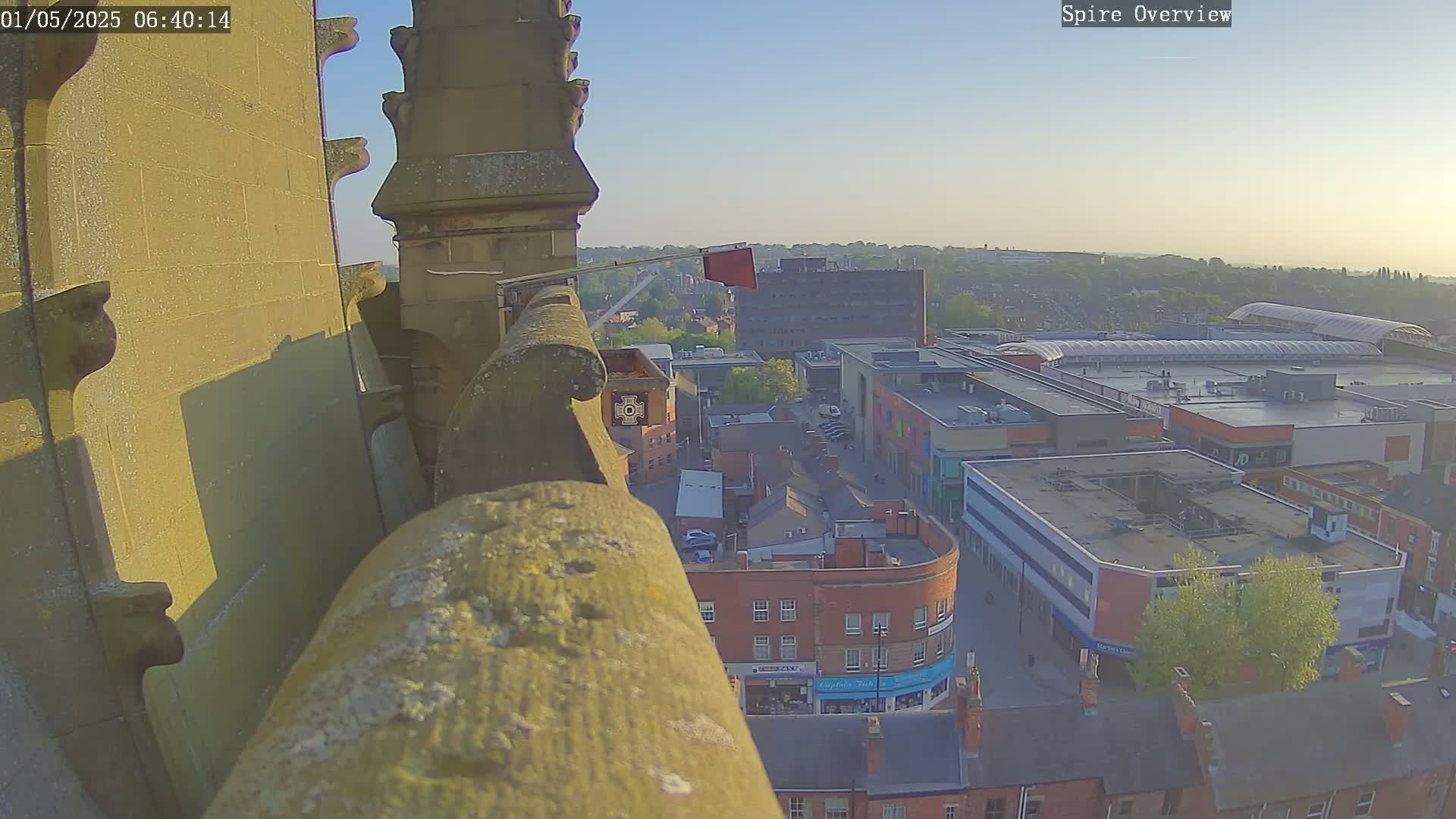 A high-angle, outdoor view at dawn shows a stone structure overlooking a town square with shops and buildings.