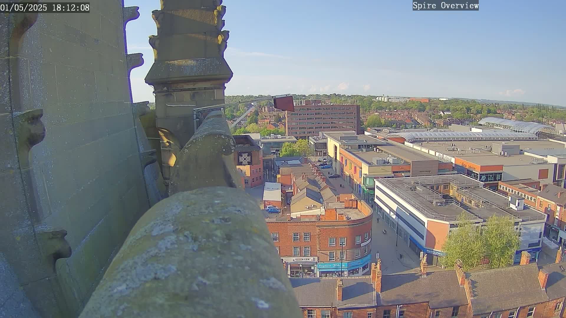 A high-angle, sunny view from a stone structure overlooking a town square and shopping center.