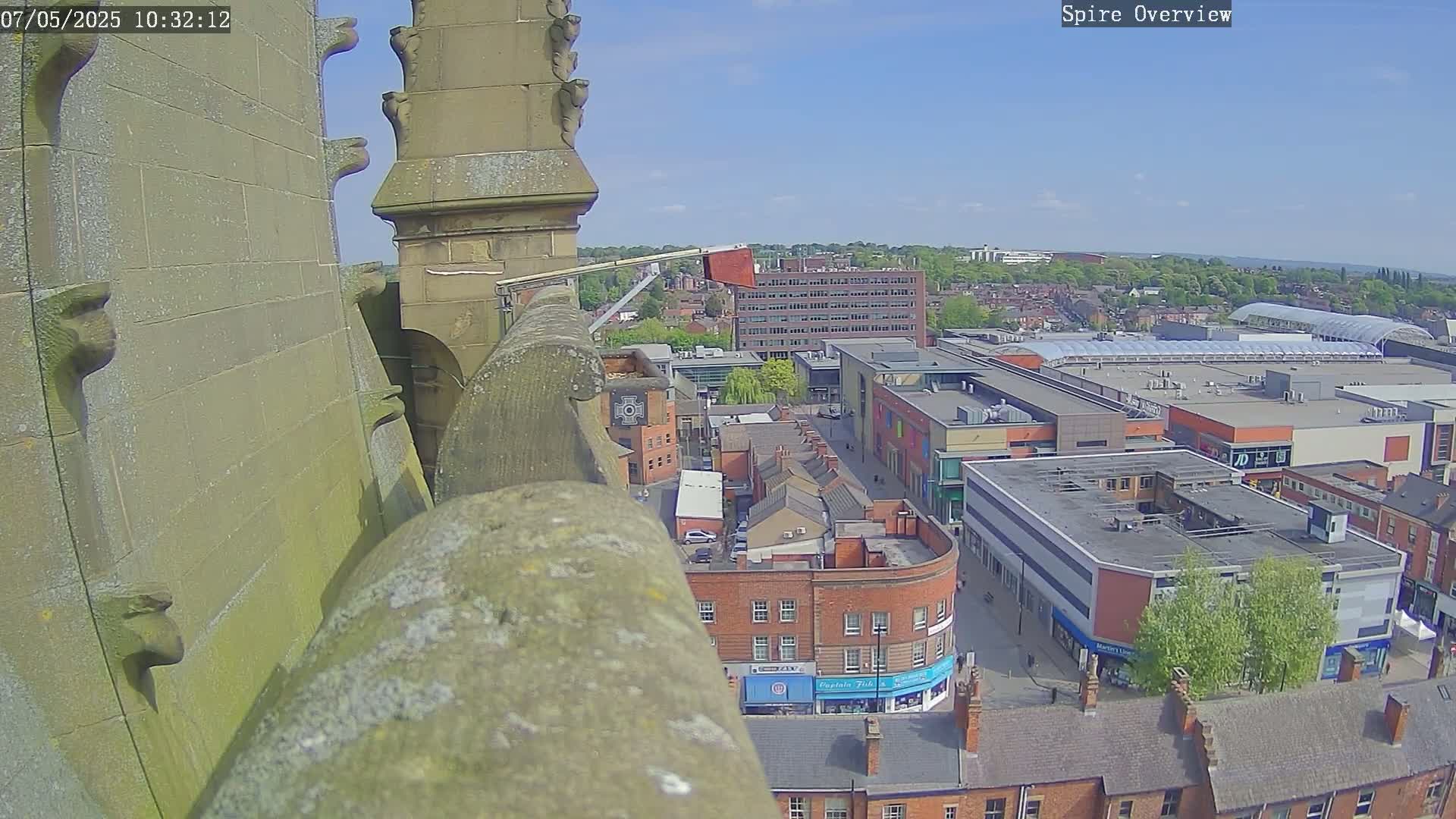 A high-angle, sunny-day view from a stone spire overlooking a town square with brick buildings and a large shopping center.