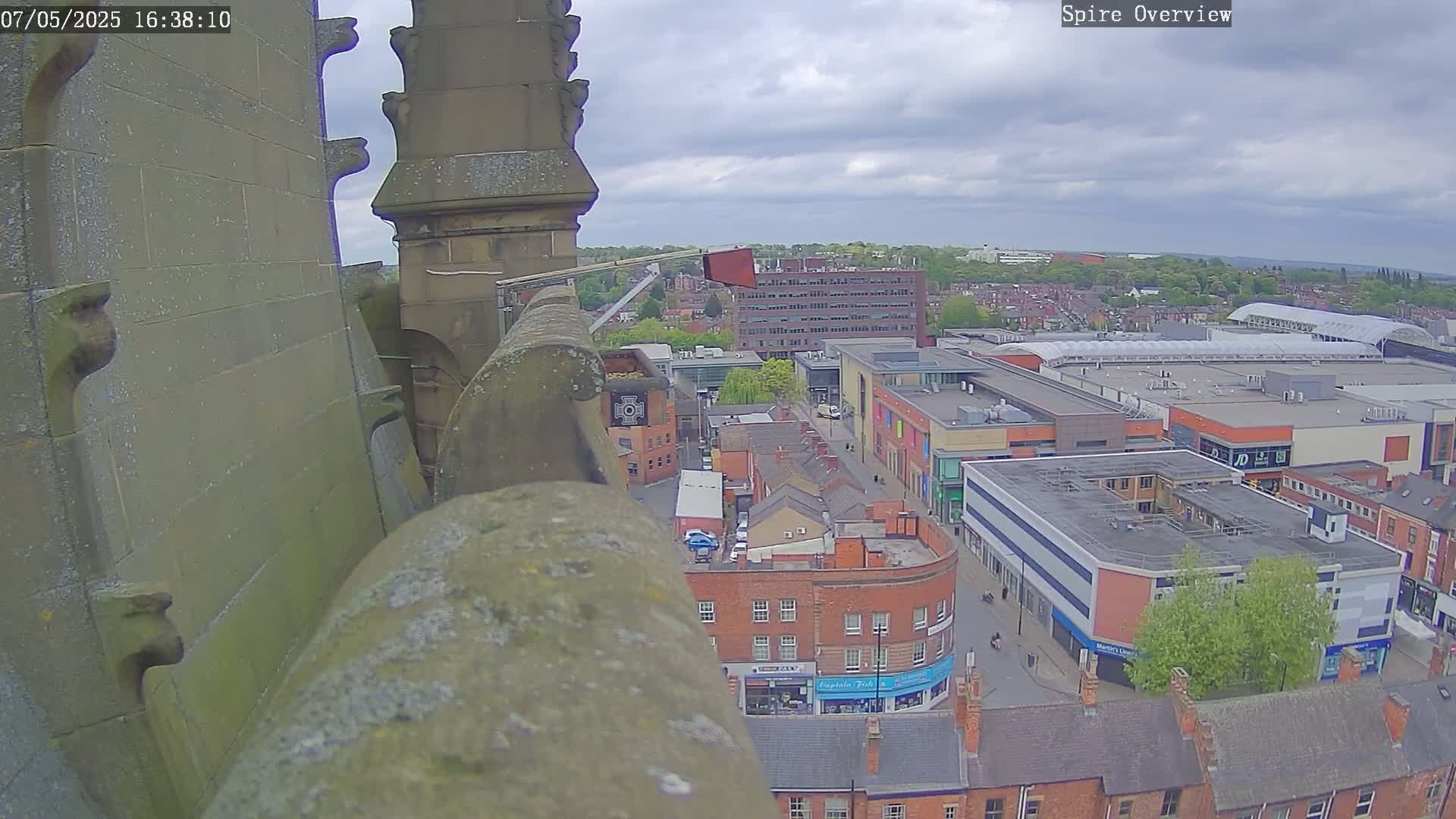 A high-angle view from a stone structure shows an overcast day over a town with a large shopping center, surrounded by brick buildings.