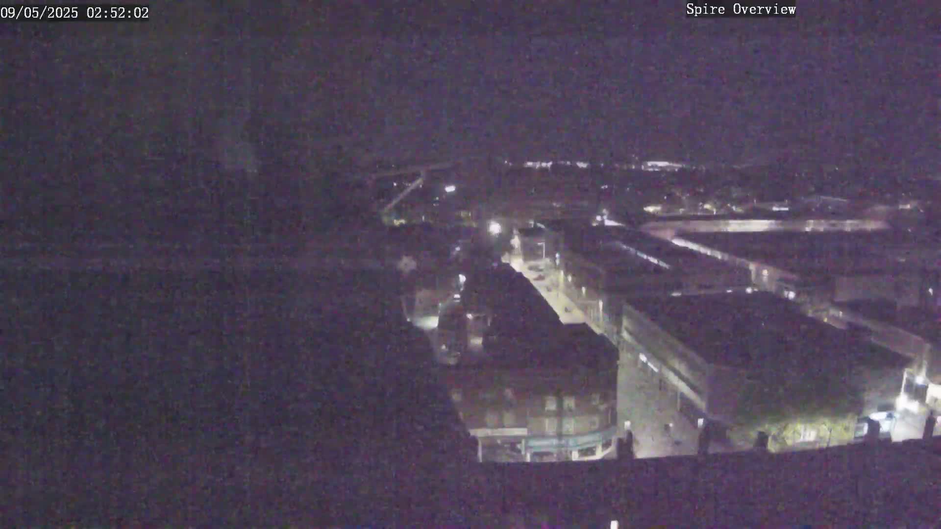 A nighttime aerial view shows a town's street and buildings illuminated by streetlights.