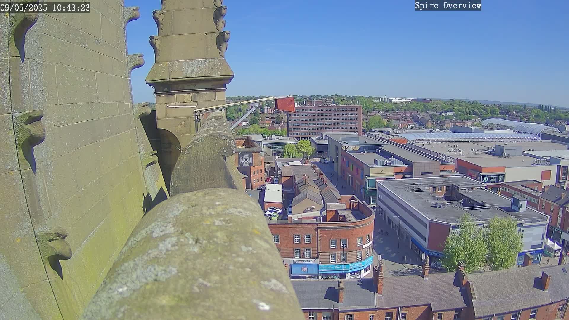 A high-angle view from a stone structure on a sunny day shows a town square with buildings and a shopping center below.