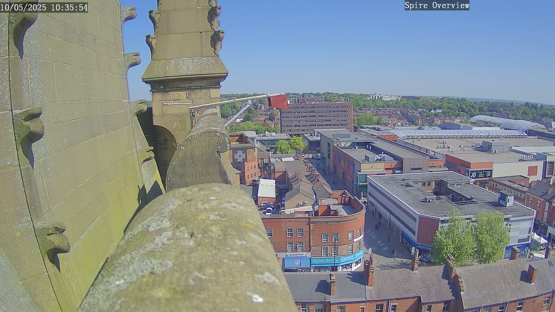 A high-angle view from a stone structure on a sunny day shows a city's cityscape, including a shopping center and brick buildings.
