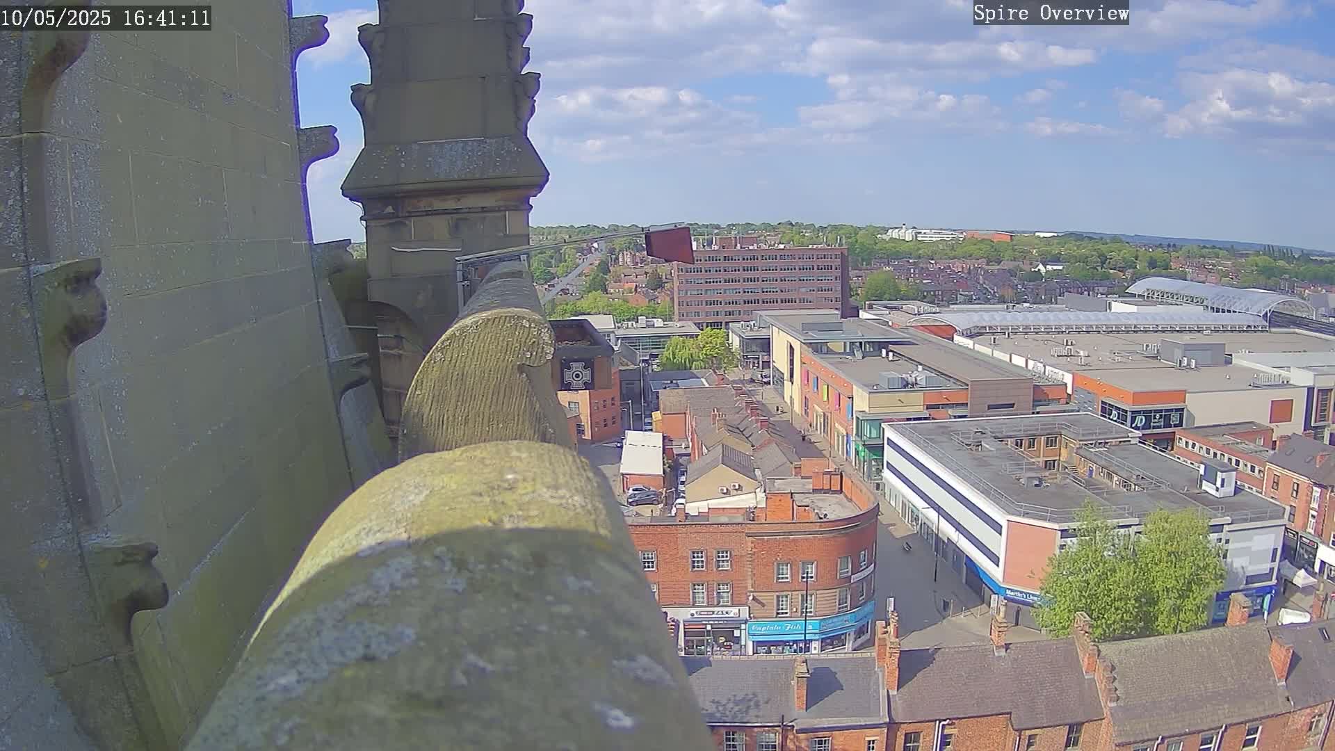 A high-angle view from a stone structure on a sunny day shows a city with buildings and a shopping center below.