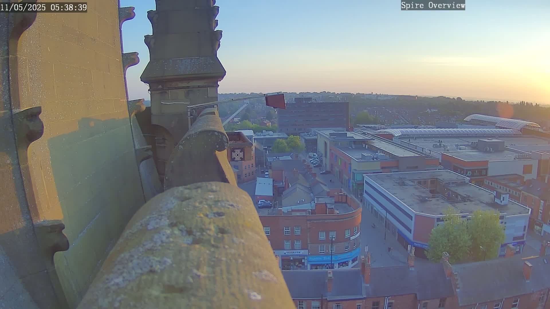 A high-angle, sunrise view from a stone structure overlooking a town with a shopping center, showing a clear sky.