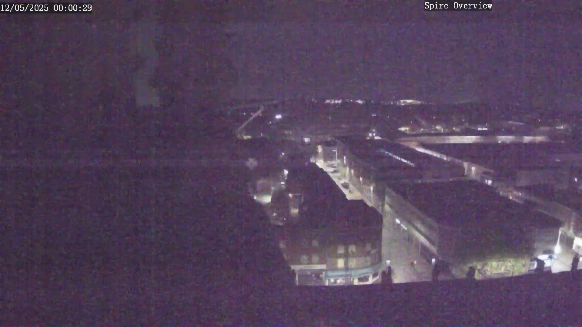 A nighttime, high-angle view shows a city street and surrounding buildings under a dark sky.