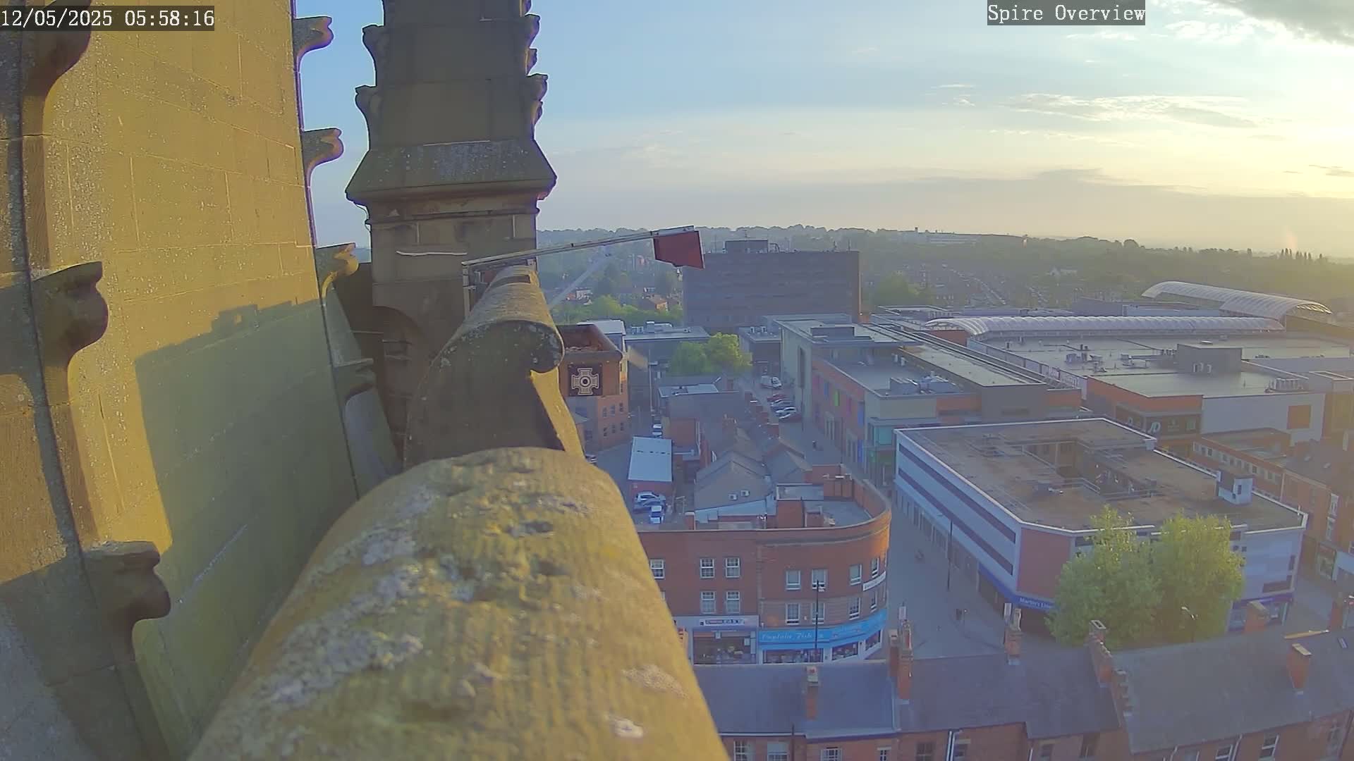 A high-angle, long shot from a stone structure overlooking a town at sunrise, shows hazy morning light over buildings and streets.