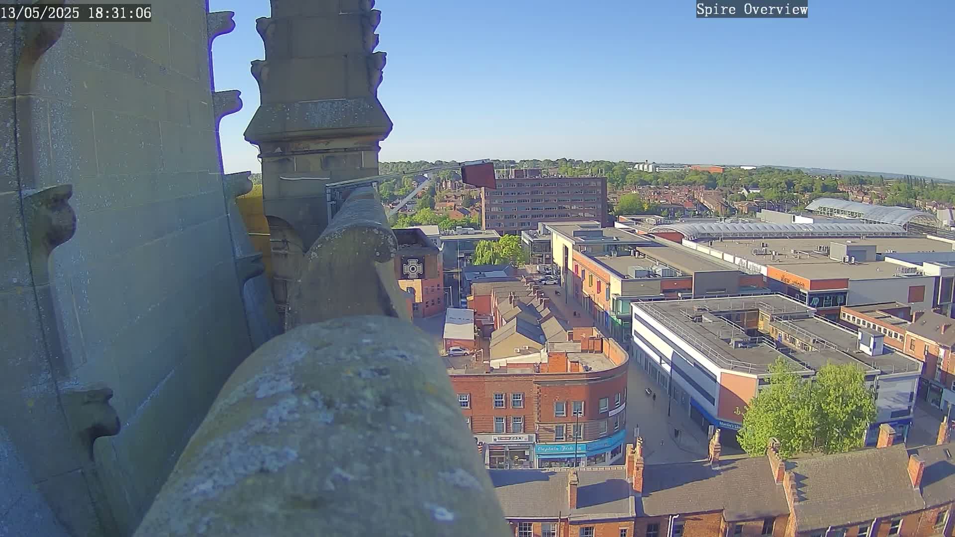 A high-angle, sunny view from a stone structure overlooking a town square and shopping center.