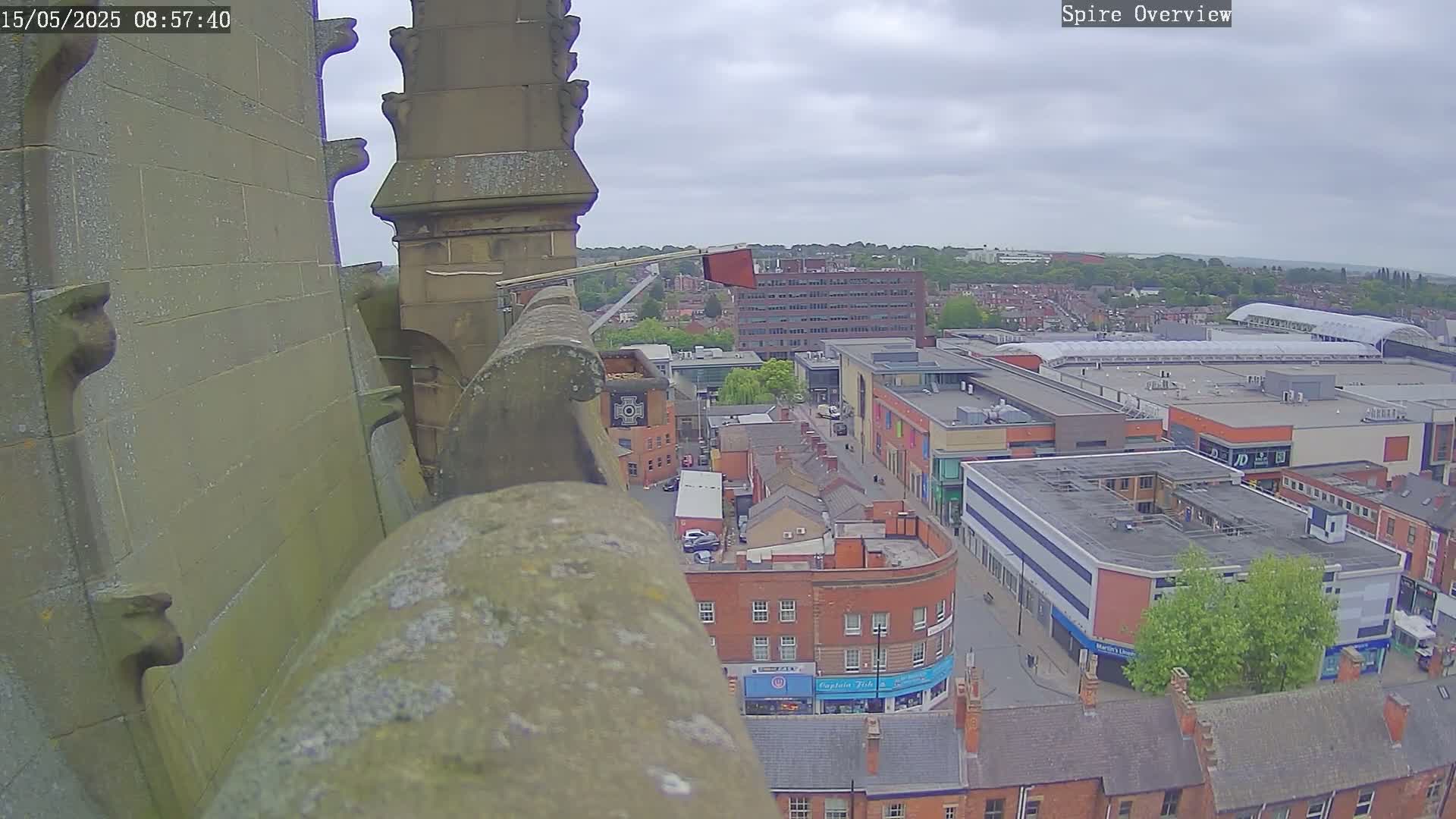 A high-angle view from a stone structure shows an overcast day over a town with a large shopping center and numerous brick buildings.