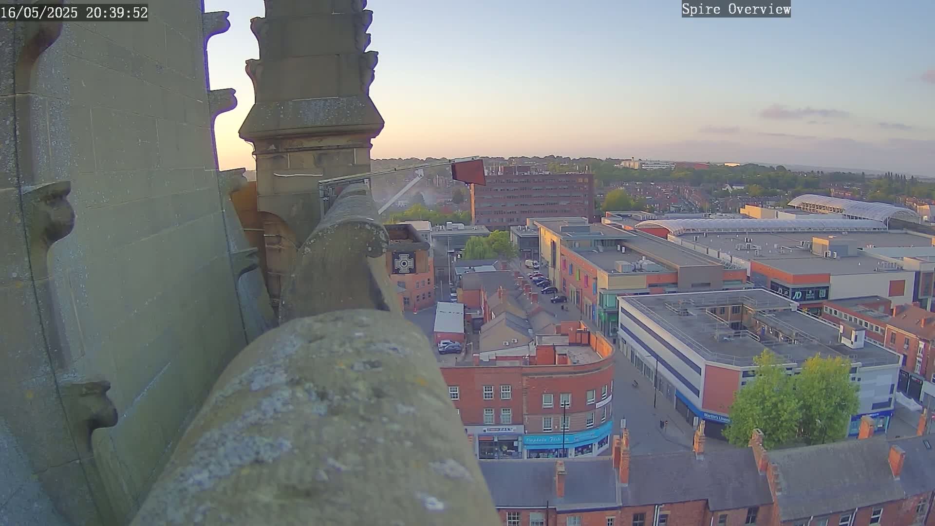 A high-angle view at dusk shows a stone structure overlooking a town square and shopping center.